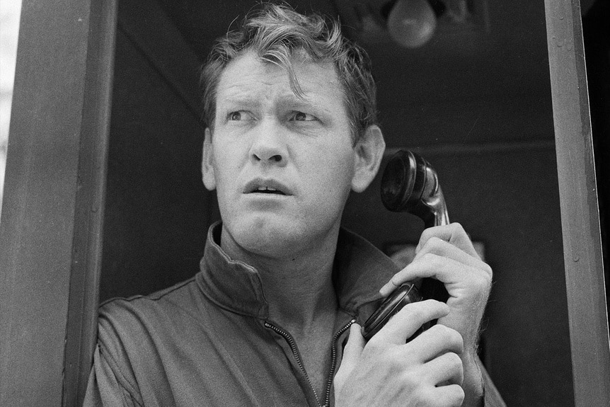 Earl Holliman holds a phone near him in a booth.