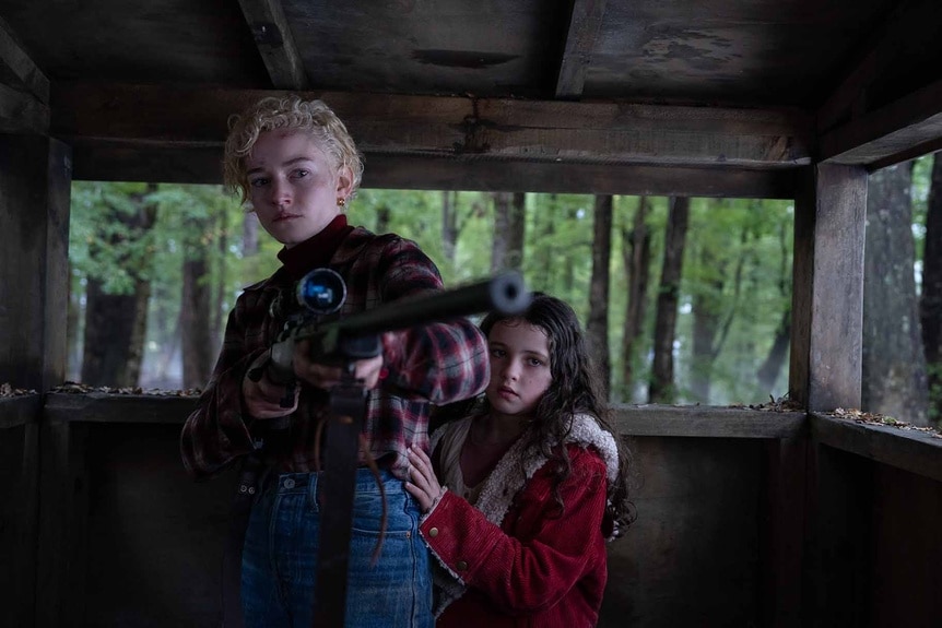 Charlotte (Julia Garner) holds a gun as Ginger (Matilda Firth) hangs on her in Wolf Man (2024).